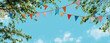 © Sher - colorful bunting and flags hanging from tree branches against a blue sky background.