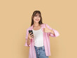 © Designerant - Happy caucasian woman holding smartphone and showing thumbs up, wearing pink shirt and white top, standing against beige studio background with copy space, approval and positive feedback concept.