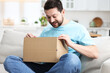 © New Africa - Happy man opening parcel on sofa at home