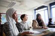 © Johnér - Girl in hijab sitting at desk with friends in classroom