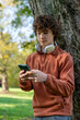 © Iryna - Young man using smartphone while standing against tree in park during daylight