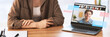 © Prostock-studio - Young manager sits at desk with laptop showing team members in a video call. She smiles at the camera while using the laptop. The workspace has a warm and inviting feel.