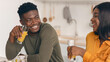 © Prostock-studio - Cheerful young black couple sitting at table and eating tasty breakfast in kitchen together, happy african american man and woman enjoying healthy food and drinking orange juice at home, closeup