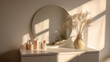 © Sevinj - A minimalist white makeup table with a large round frameless mirror reflecting a sun-lit room. On the table, pastel-colored skincare bottles and a single ceramic vase with dried flow