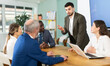 © JackF - Man stands in front of business colleagues, tells report, proves vision of situation, defends way to solve problems. People are sitting at table, and participant is standing up and took floor. .