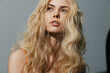 © VICHIZH - Elegant young woman with wavy blonde hair in soft lighting, showcasing a serene expression and natural beauty, ideal for fashion and beauty concepts.