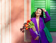 © VISTA by Westend61 - Smiling woman holding tulips in vibrant purple coat outdoors