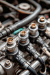 © Anoo - Close-up of a car engine shows metal clamps securing various washers and rubber connectors. Water pipes connect to an electrical device in a blurred setting