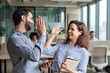 © insta_photos - Two happy friendly diverse professionals, teacher and student giving high five standing in office celebrating success, good cooperation result, partnership teamwork and team motivation in office work.