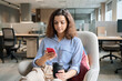 © insta_photos - Hispanic latin young woman student holding smartphone and coffee sitting in modern space studying on cell, browsing, checking apps, texting using mobile phone in university campus or creative office.