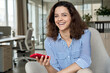 © insta_photos - Happy hispanic young woman laughing holding smartphone, portrait. Smiling latin teen girl student having fun enjoying using modern mobile apps on cell phone tech sitting in chair looking at camera.