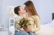 © New Africa - Little boy greeting his mom with flowers on bed at home