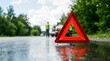© Norah Allen - Red triangular warning sign placed on a wet road with a broken down car and tow truck visible in the distance warning triangle car breakdown roadside assistance emergency