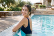 © Meow Creations - Young woman in dark swimsuit relaxing and smiling gracefully in a luxurious outdoor swimming pool