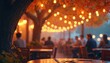 © Lubov - Outdoor cafe tables with warm string lights and autumn leaves overhead. People sit at tables in blurred background. Dusk creates cozy ambiance.