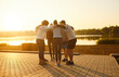 © Studio Romantic - Group of sporty fit friends people huddling together outdoors by lake at sunrise, arms around showing unity and support, strong connection and shared purpose, teamwork bonding mutual encouragement
