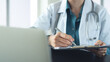 © tippapatt - Doctor writing on medical document, medical report on clipboard with laptop on office desk