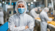 © Puthorn - Front view of confident employee wea protective suit and face mask standing with crossed arms at food manufactu factory floor
