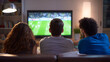 © photo for everything - Diverse Group of Friends Gather to Watch Competitive Sports Game on Television in Cozy Living Room at Night, Rear View