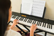 © AntonioDiaz - Young woman learning to play keyboard, practicing digital piano with sheet music in home setting