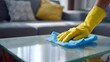 © PALLU GOLLA - Close-up of a hand wearing a yellow glove, wiping a glass table with a blue cloth for cleaning