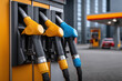 © Keopaserth - Yellow and blue fuel nozzles at modern fuel pump station with forecourt canopy and blurred car in background conveying refueling scene and urban service convenience