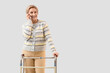 © Pixel-Shot - Mature woman with walker talking by mobile phone on light background