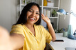 © Daniel - Latin woman waving hand and taking selfie at home office desk