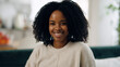 © DMegias - Happy African American woman with curly hair smiling directly at camera while relaxing comfortably inside her home