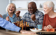 © Prostock-studio - Emotional black man playing chess with multiracial friends, happy elderly men and women in casual outfits sitting around table with table games, chatting, having fun at sanatorium
