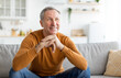 © Prostock-studio - Portrait of cheerful casual senior man smiling and looking away, sitting on sofa couch in living room. Excited grandfather resting at home dreaming about something pleasant, free copy space