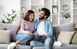 © Prostock-studio - Happy positive beautiful loving young indian couple man and woman spending time together at home, sitting on couch in cozy living-room, embracing and laughing, lovers have conversation