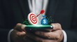 © MDMITHAN - Businessman holding smartphone with target and dollar sign icons for finance and investment goals