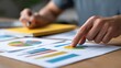 © KKC Studio - Analyzing the Data: A close-up shot of a person's hands meticulously analyzing financial charts and graphs, pointing to a key data point with focused attention.