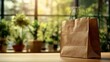 © sornram - A natural light setting showcases a brown paper shopping bag on a wooden table, surrounded by lush green plants.