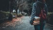 © Ameer - Back view of student holding books while walking on campus path, outdoor education scene, face not visible