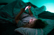 © Volodymyr - Child holding smartphone under blanket light. Kid using technology during bedtime routine. Child watching video on phone at night. Kid scrolling content on mobile device in bed.
