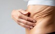 © NovaVision - Close-up of a woman's hand touching wrinkled skin on her abdomen, showing signs of aging