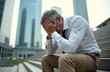 © Pete - Elderly man sits on city stairs head in hands. He wears formal shirt and trousers. Buildings are blurred in background. Mature person looks stressed and upset. Sad businessman has problems.