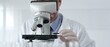 © rogerphoto - Scientific researcher wearing lab coat, glasses and white protective gloves carefully calibrating laboratory microscope, performing precision medical investigation. Medicine, healthcare and science