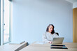 © we.bond.creations - Confident businesswoman with gray hair using a laptop, focusing on work at her desk in a bright, contemporary office space