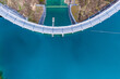 © AmazingAerialAgency - Aerial view of the Klaus Dam curving gracefully over the turquoise waters, a stark contrast to the rugged, brown landscape, Klaus an der Pyhrnbahn, Oberosterreich, Austria.