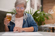 © luciano - Smiling senior woman sitting at restaurant table while choosing what to eat from menu