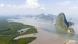 © AmazingAerialAgency - Aerial view of limestone karsts rising from the calm sea and lush mangrove forests under a bright sky in Phang Nga, Thailand.