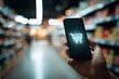 © Marie - Hand holding phone with shopping cart symbol in supermarket aisle. Blurred background