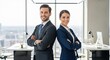 © Khan - A confident man and a professional woman stand back-to-back in a modern office setting. They are both dressed in business attire, wearing suits and ties.