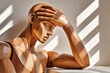 © Georgii - Wooden mannequin holding its head in hand expressing stress and contemplation in sunlit studio