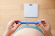 © Oleg - A horizontal close up of a young woman holding pre-filled pen injector with semaglutide A young woman holding pre-filled pen injector with semaglutide on floor and scales background