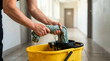 © Xenia - Janitor hands wringing a wet green mop over a yellow bucket. Close-up of water dripping during floor cleaning. Commercial sanitation and maintenance labor concept