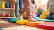 © Taras Roshchuk - A child practices balance on colorful sensory pads in a therapy room. Adults support and observe the child's movements. This activity aids in physical development and coordination